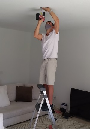 About handyman, drilling something staying on the ladder.