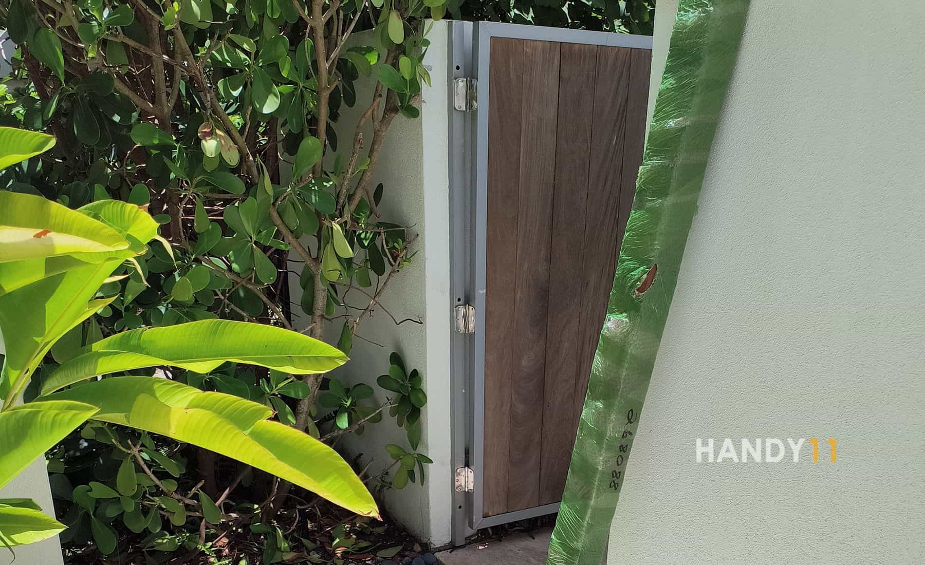 White concreete fence, brown wood entrance door repair, IPE post, green plants around.