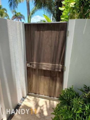 White concreete fence and Brown wood entrance door from inside point of view. Green plants around.