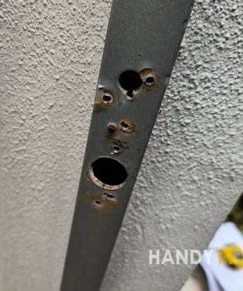 Metal square pipe with a number of holes fixed on white concrete wall.