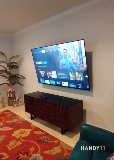 Big TV mounted, red rug, brown wood tv-stand in living room.