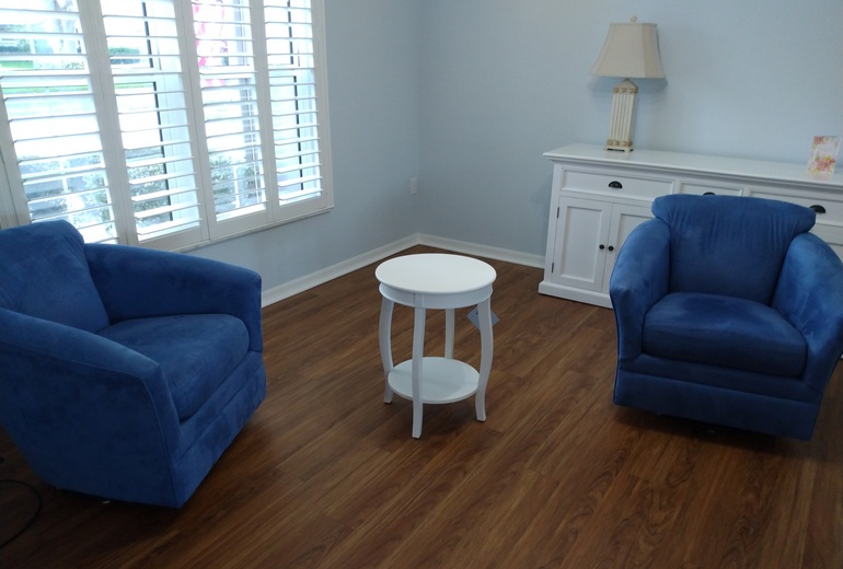 Blue soft chairs and white end table assembled on brown wood floor.