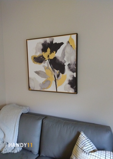 Square Art Picture in the frame mounted on the wall above grey leather couch.
