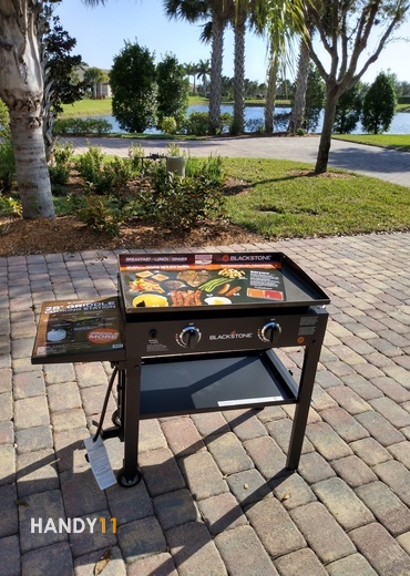 Blackstone griddle assembly. Griddle assembled on driveway with palmtrees and pond behind.